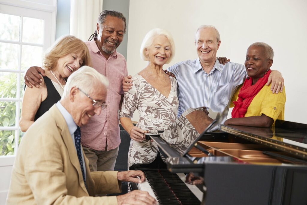 Friends standing around a piano watching a man play